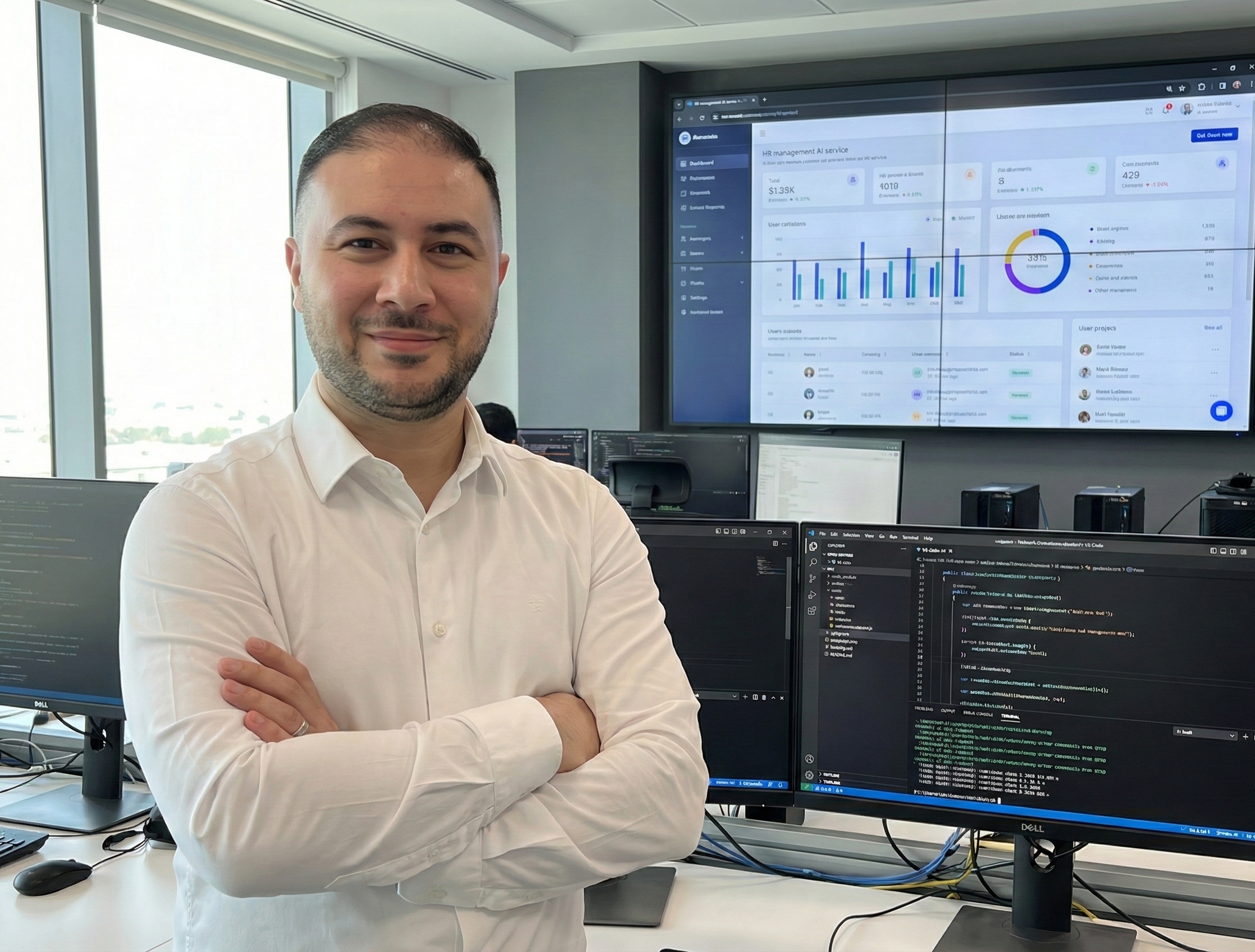 Mann in weißem Hemd mit verschränkten Armen vor mehreren Computermonitoren mit Programmiercode und Datenanzeigen in einem modernen Büro.